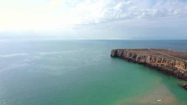 Spectacular coastline of Portugal. View of Sagers cape and lighthouse. Drone ascending. Fanous travel destination. Turquoises water colour. Cloudy sky.