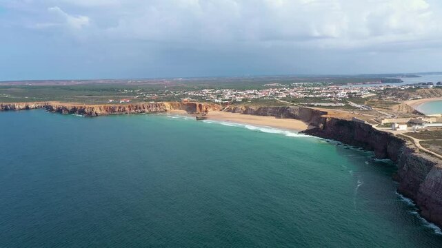 Tonel Beach, natural beach situated in in South of Portugal, Sagres. High cliff, Sagers city in background. Famous travel destination for water sports. drone going forward descending. Surfers in water
