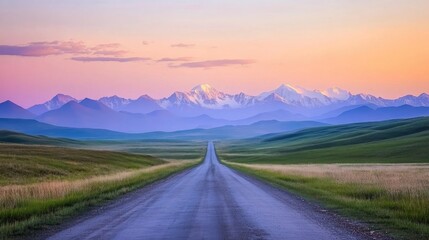 Fototapeta premium Serene rural road stretching through lush grassy fields with majestic mountains bathed in soft sunrise light creating a tranquil landscape.