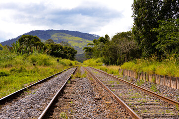 Obraz premium Railway tracks extending into the distance, surrounded by natural scenery. The focus highlights the metal rails and gravel bed, with parts of the background gently blurred for depth.