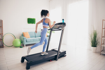 Young woman exercising on treadmill in modern apartment with sunlight and vibrant decor, promoting...