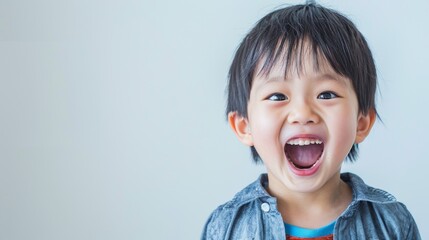 A young boy with dark hair and a denim shirt open-mouthed and laughing.