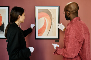 Gallery staff dressed in dark and casual attire, discussing modern abstract painting hanging on...