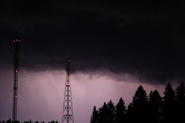 Naklejka premium Lightning during a night thunderstorm near a forest and two television towers.