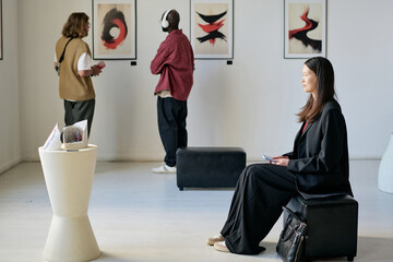 People of different backgrounds enjoying an art gallery with abstract paintings. Artwork displayed...