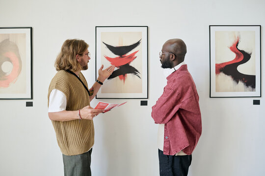Two men talking and analyzing abstract artwork in modern gallery setting. They are paying close attention to the details and discussing perspective techniques