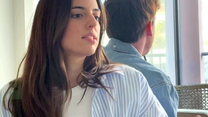 A young woman sitting on a sofa, visibly upset, while a man sits with his back to her, discussing issues related to their relationship, including emotional distance and possible breakup relationship