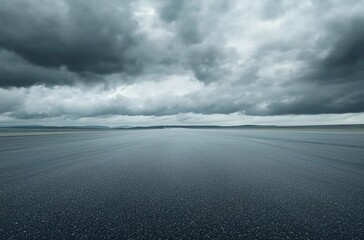  A wide shot of an empty asphalt racetrack with dark gray clouds in the sky.