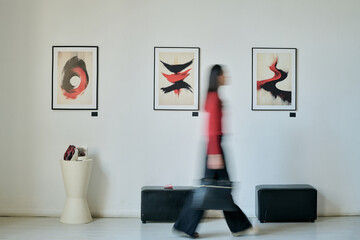 Individual with blurred figure walking past modern art pieces in gallery creating sense of motion,...