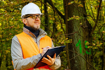 European man in a helmet with a tablet checking trees. Eco volunteer. Male environmental technician...