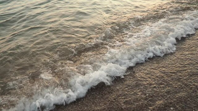 Waves gently lap at shore during stunning sunset over ocean. Golden sunlight reflects off waves as they roll onto shore, creating tranquil atmosphere at sunset by sea. Montenegro summer, Canj