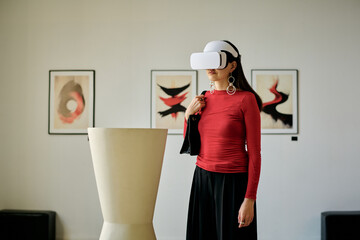 Woman interacting with virtual reality headset standing in contemporary gallery. Observing...
