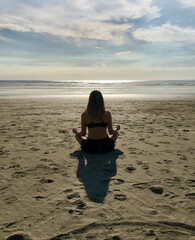 Girl sitting and meditating alone on a beach at sunset