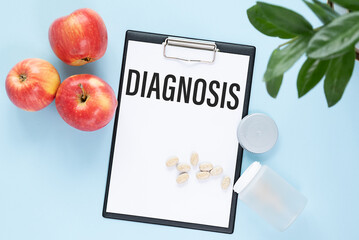 Paper with text DIAGNOSIS on a blue background with apples and pills