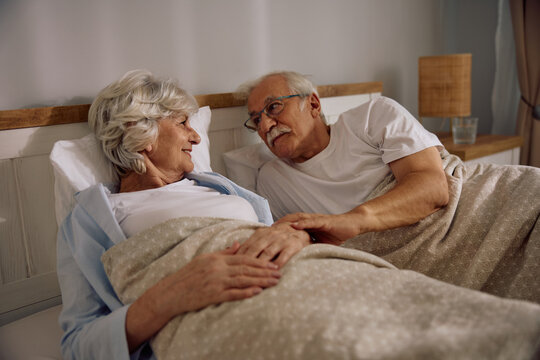 Smiling senior couple talking while lying down in bed. - Powered by Adobe