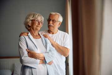 Portrait of smiling senior couple by window in their bedroom.