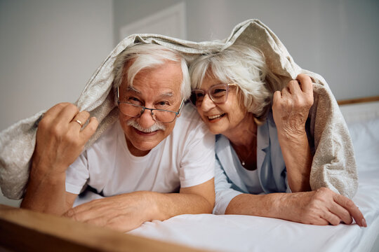 Carefree senior couple having fun in bedroom and looking at camera.
