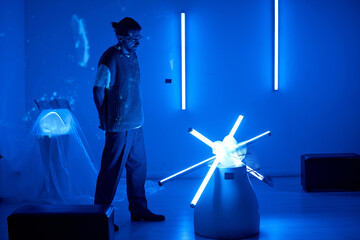 Individual admiring contemporary art installation in dimly lit room with blue lights ambient. Modern sculpture illuminated by LED lights forming a star-like pattern