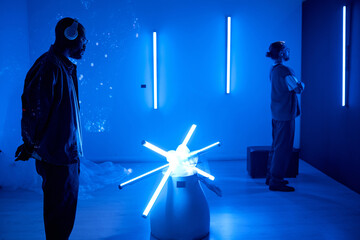 Individuals enjoying a futuristic art installation in a dark room illuminated by neon lights Both people are wearing headphones, enhancing their immersive experience