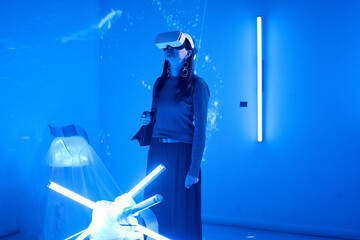 Person using virtual reality headset in a blue-lit futuristic room with modern lighting features and advanced technology setup creating an immersive environment