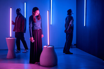 Individuals observing light sculptures in modern art gallery with neon blue and pink lighting creating an immersive, thoughtful environment - Powered by Adobe