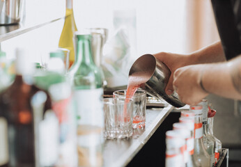 Bartender pours a prepared drink from a shaker into a glass, disco, beach bar, alcohol, alcoholism,...