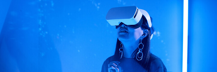 Woman wearing VR headset enjoying an immersive virtual reality experience, illuminated by a deep...