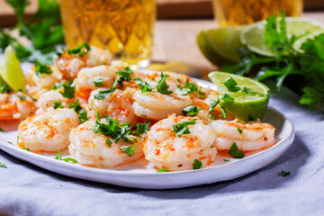 Shrimp cooked with garlic and herbs, served with beer and lime on a wooden table.