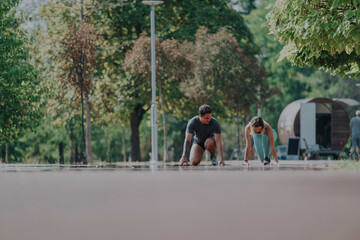 Two friends are stretching on a park path, preparing for a run on a sunny day. Trees and greenery provide a lively backdrop, emphasizing fitness and outdoor wellness.