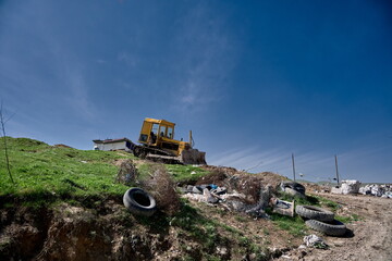  bulldozer stands on a grassy, debris-covered hill.