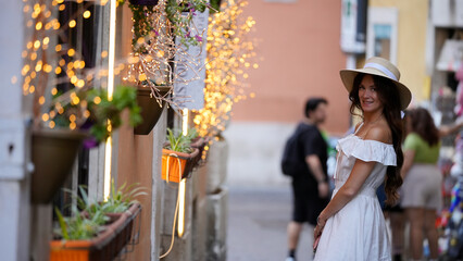 A fashionable traveler pauses to admire illuminated flowers and festive lights, capturing the charm...