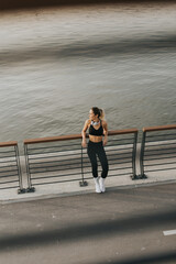 A confident athlete enjoys a moment of reflection while stretching on a riverfront path during golden hour