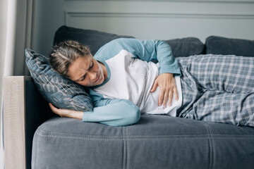 Woman lying on sofa at home has stomach pain, menstruation, stomach ache