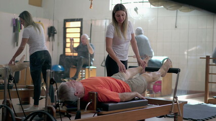 Pilates coach guiding a senior man in machines. Older person strengthening body in workout routine