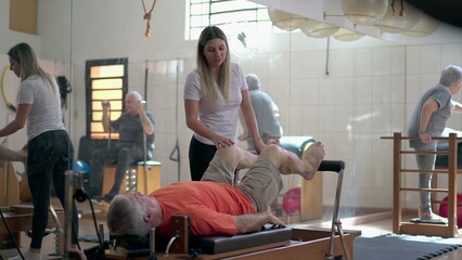 Pilates coach guiding a senior man in machines. Older person strengthening body in workout routine