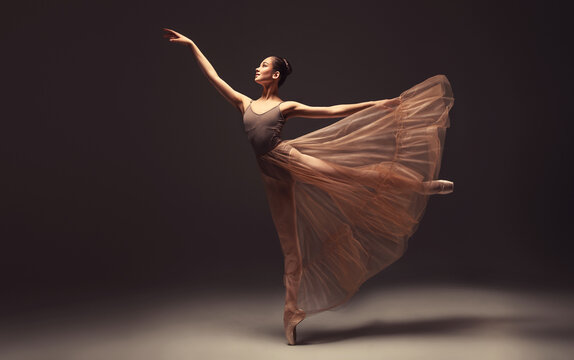 Ballerina. Young graceful woman ballet dancer, dressed in professional outfit, shoes and beige weightless skirt is demonstrating dancing skill. Beauty of classic ballet. - Powered by Adobe
