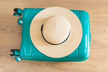 Lying on floor a bright green travel suitcase with a straw hat on top is full of  summer vacation clothes lying on floor. Overhead view.