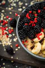 Oatmeal with red ripe blackberries and bananas in the bowl. Selective focus.