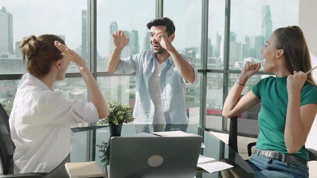 Professional business team receive a good news by using laptop while celebrate their success. Manager pointing at laptop while high five and clap hands with colleague at modern office. Tracery