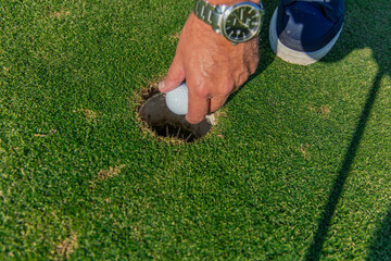 closeup senior golfer's hand with wristwatch retrieving golf ball from hole on the green