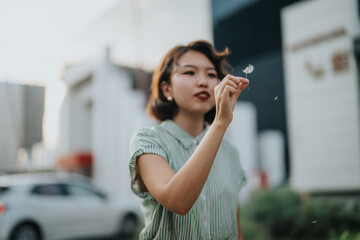 A young Asian woman stands outdoors in a busy city area, holding a dandelion seed head. She appears...