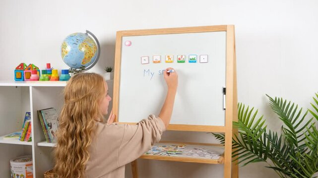 A young girl, a child is having fun learning to build sentences using magnetic word tiles and frames on a whiteboard in a classroom.