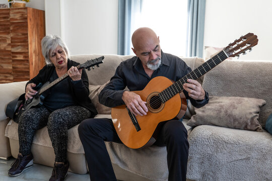 Couple, 70 years old, playing guitar on the sofa in their living room. Woman electric, Man, acoustic