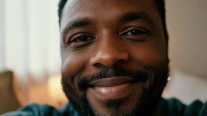 Warm smile of a black man evolves into joyous expression in living room setting.