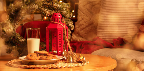 Christmas cookies with glass of milk and decor on table in room at night, closeup