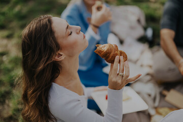 A group of multiracial friends enjoying a peaceful picnic in nature, savoring pastries and conversation under a cloudy sky. The atmosphere is casual and serene, perfect for relaxation.