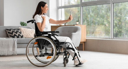 Young woman in wheelchair using mobile phone at home