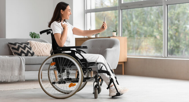 Young woman in wheelchair using mobile phone at home