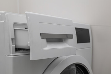 Modern washing machine with open detergent drawer near light wall, closeup