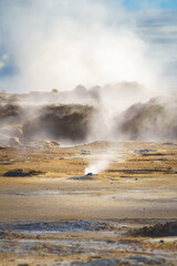 Sulfuric steam vents in the Hverir geothermal area of Námafjall, Iceland, emitting clouds of vapor on a barren landscape.